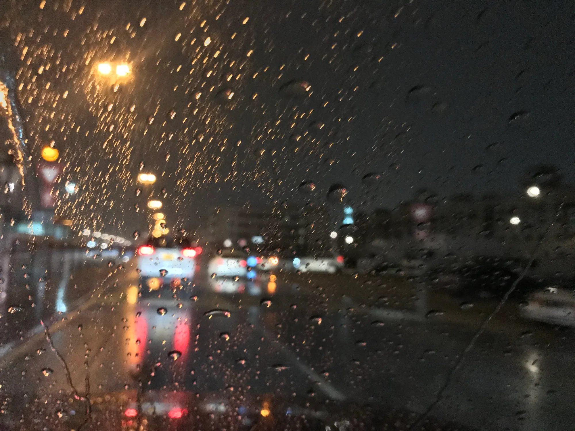 Rain on a car windscreen at night on a Dubai road, with tail lights ahead
