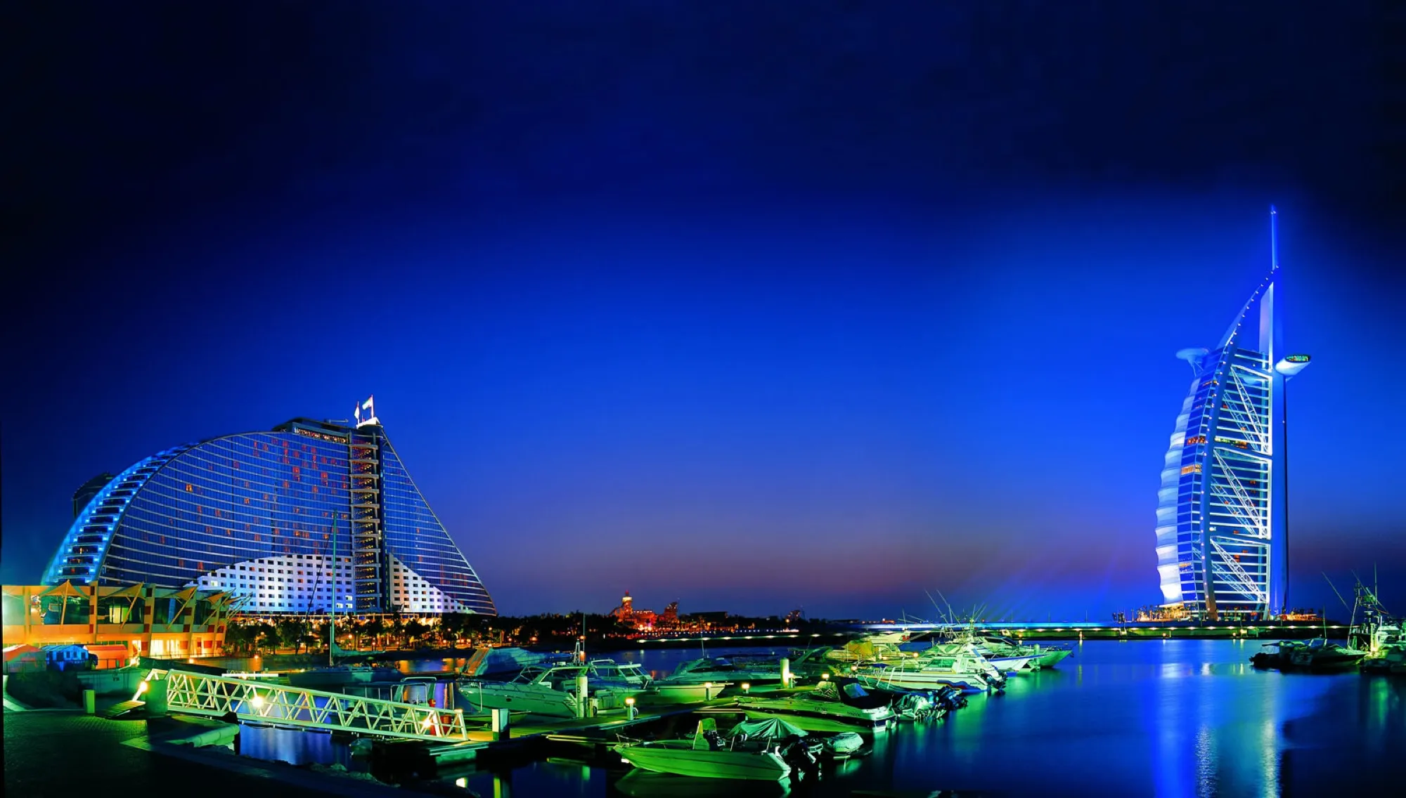 Jumeirah Beach Hotel and the Burj Al Arab lit up at night across the water in Umm Suqeim