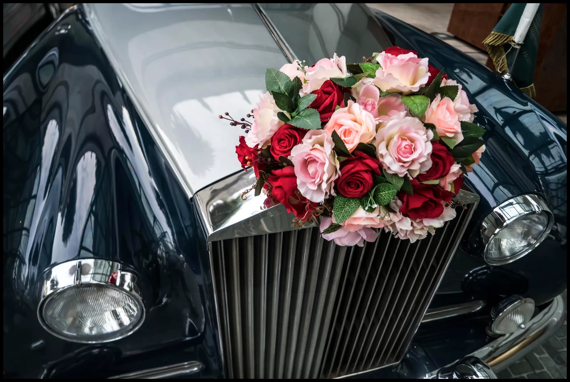 Pink and red roses fixed to the bonnet of a black Rolls-Royce, just above the grille