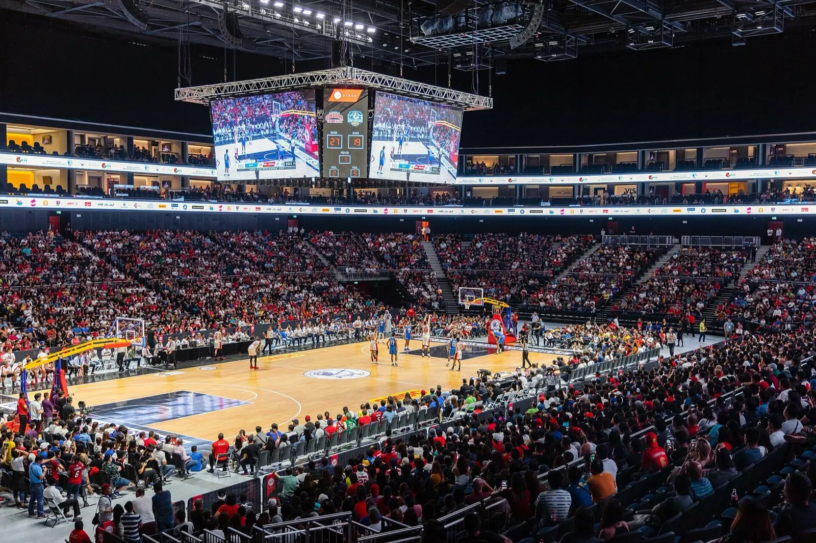 A full crowd watching a basketball game inside Coca-Cola Arena, with the large video board hanging above the court