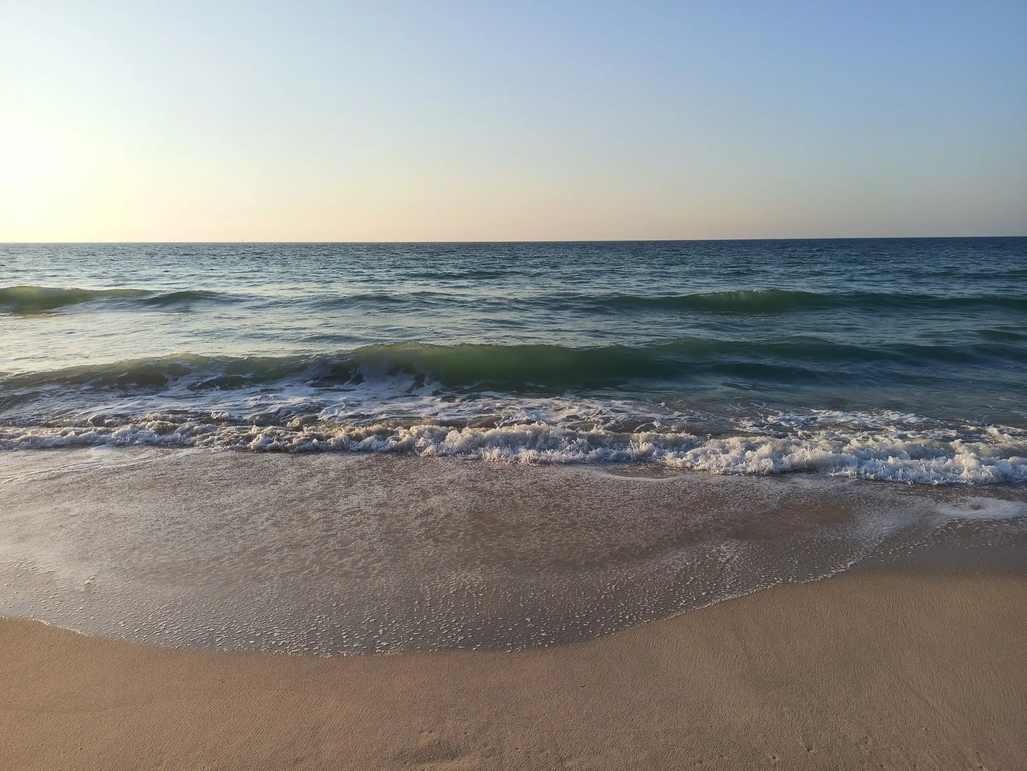 Waves reaching the sand on the Ajman beach at sunset