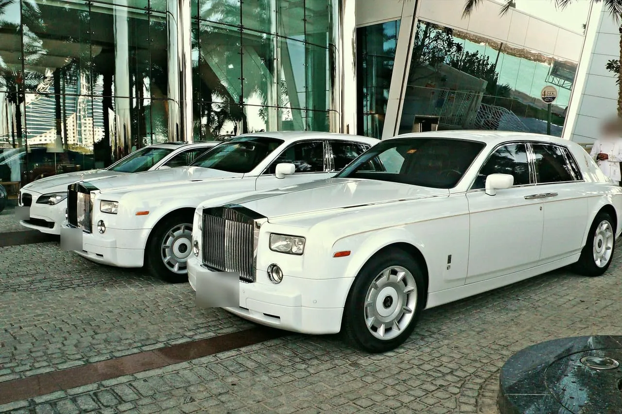 Two white Rolls-Royce Phantoms and a white BMW parked at a hotel entrance in Dubai