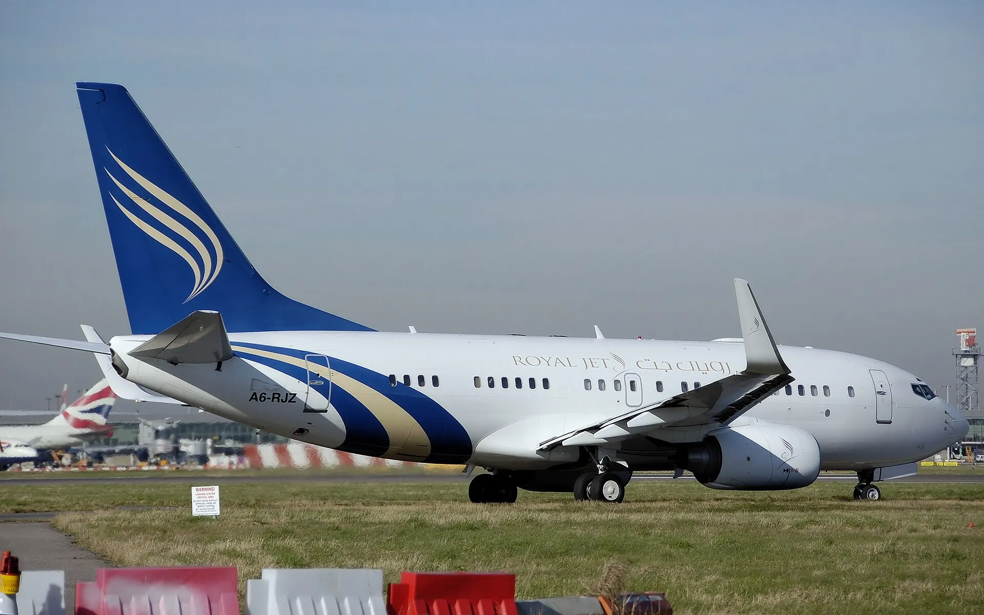 A white Boeing business jet with a blue tail taxiing on an airport apron