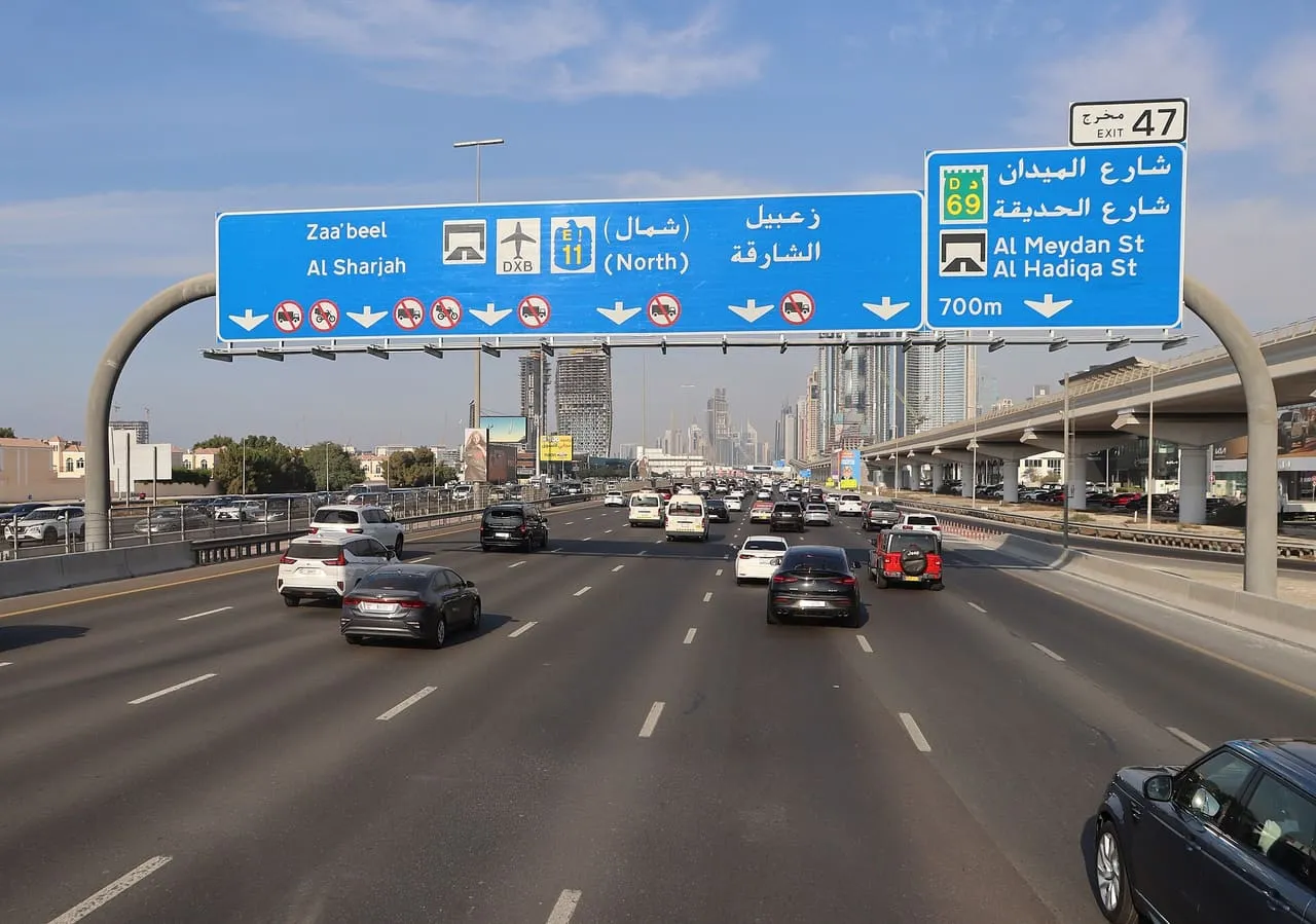 Traffic on Sheikh Zayed Road in Dubai under an overhead sign for Exit 47, with the Metro line running alongside