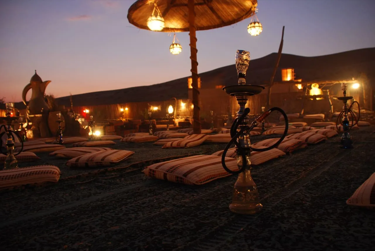Floor cushions, shisha pipes and hanging lanterns laid out at a desert camp outside Dubai at dusk