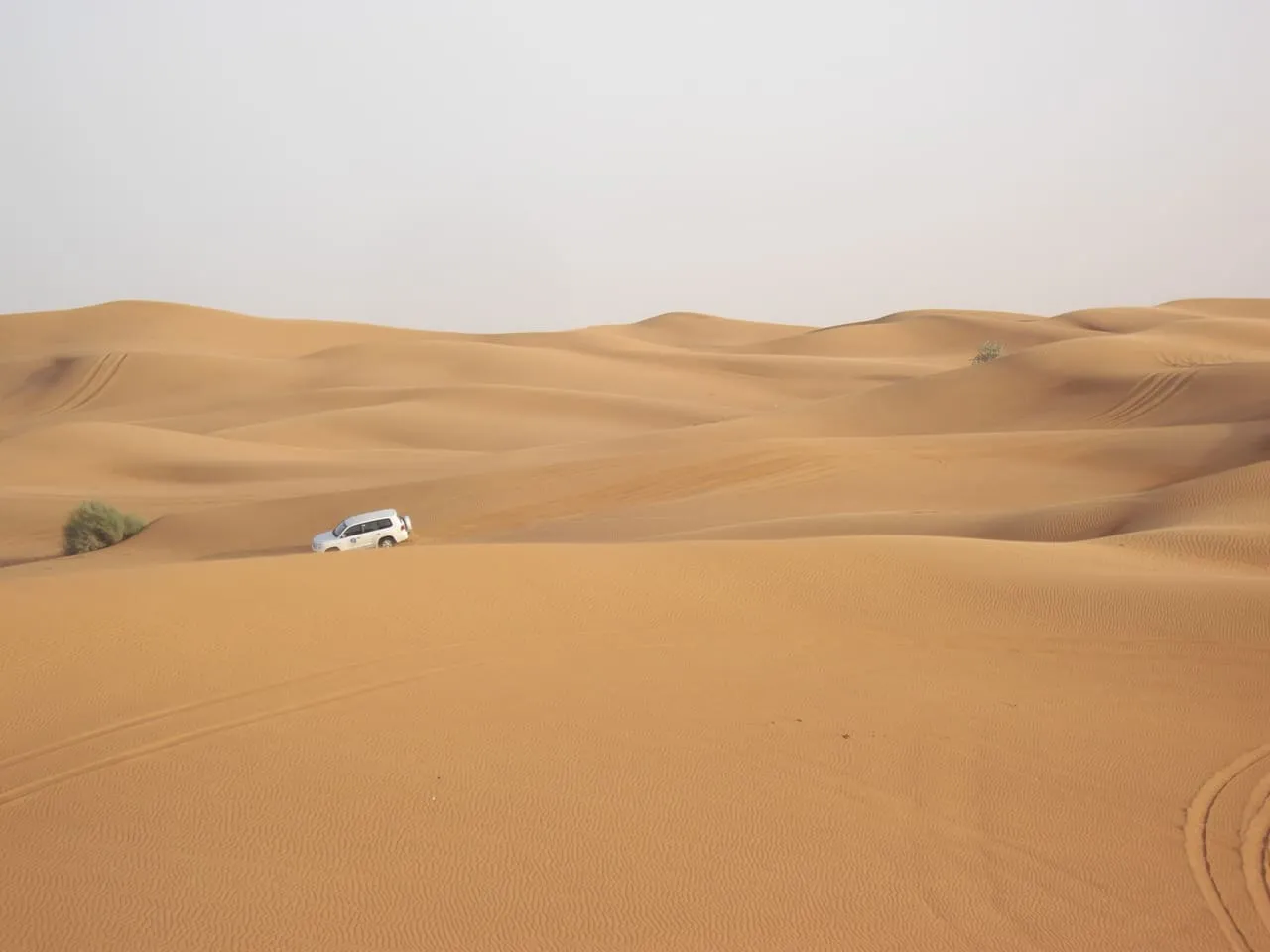 A white 4x4 crossing wide orange dunes in the desert outside Dubai