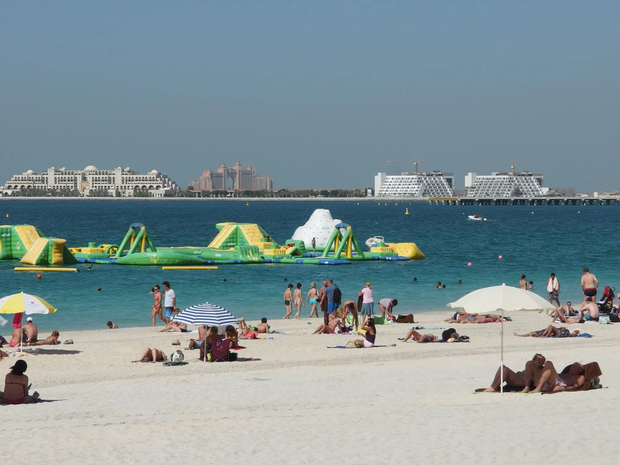 Families and swimmers on the white sand of the beach at Jumeirah Beach Residence, with Atlantis on Palm Jumeirah across the water