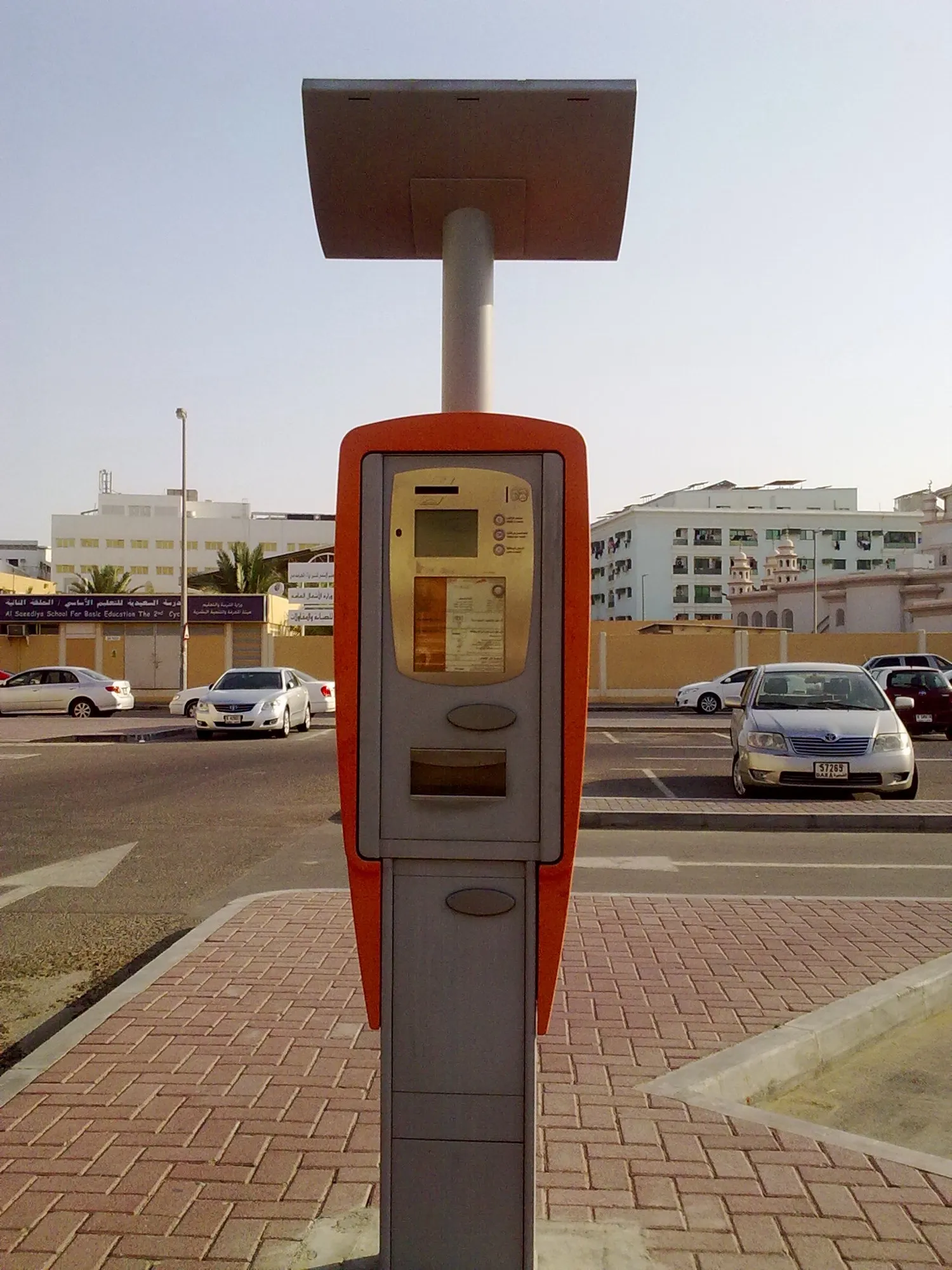 A Dubai pay-and-display parking machine beside a parking lot with cars