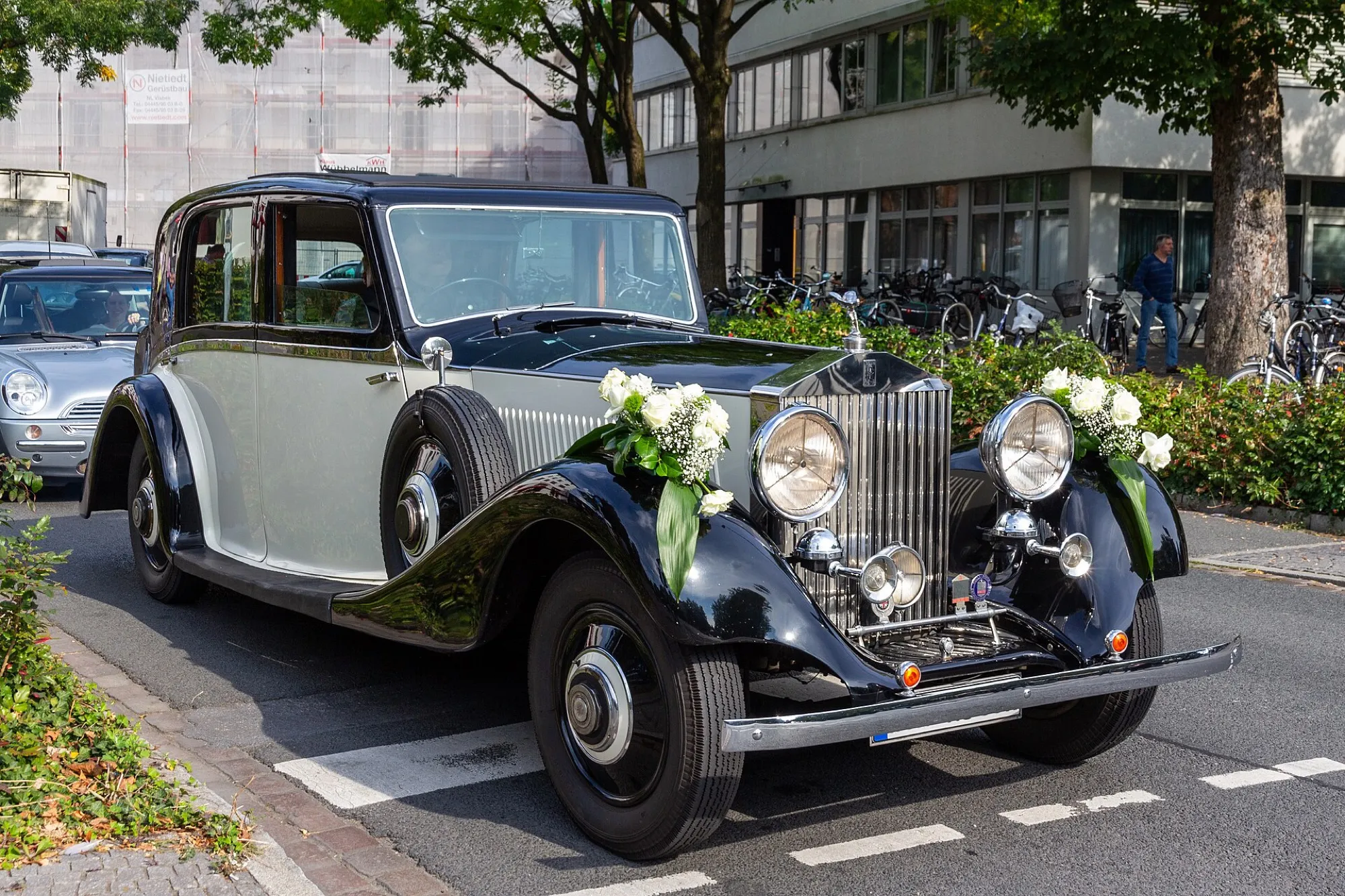 A vintage Rolls-Royce with bouquets of white roses fixed to the front wings
