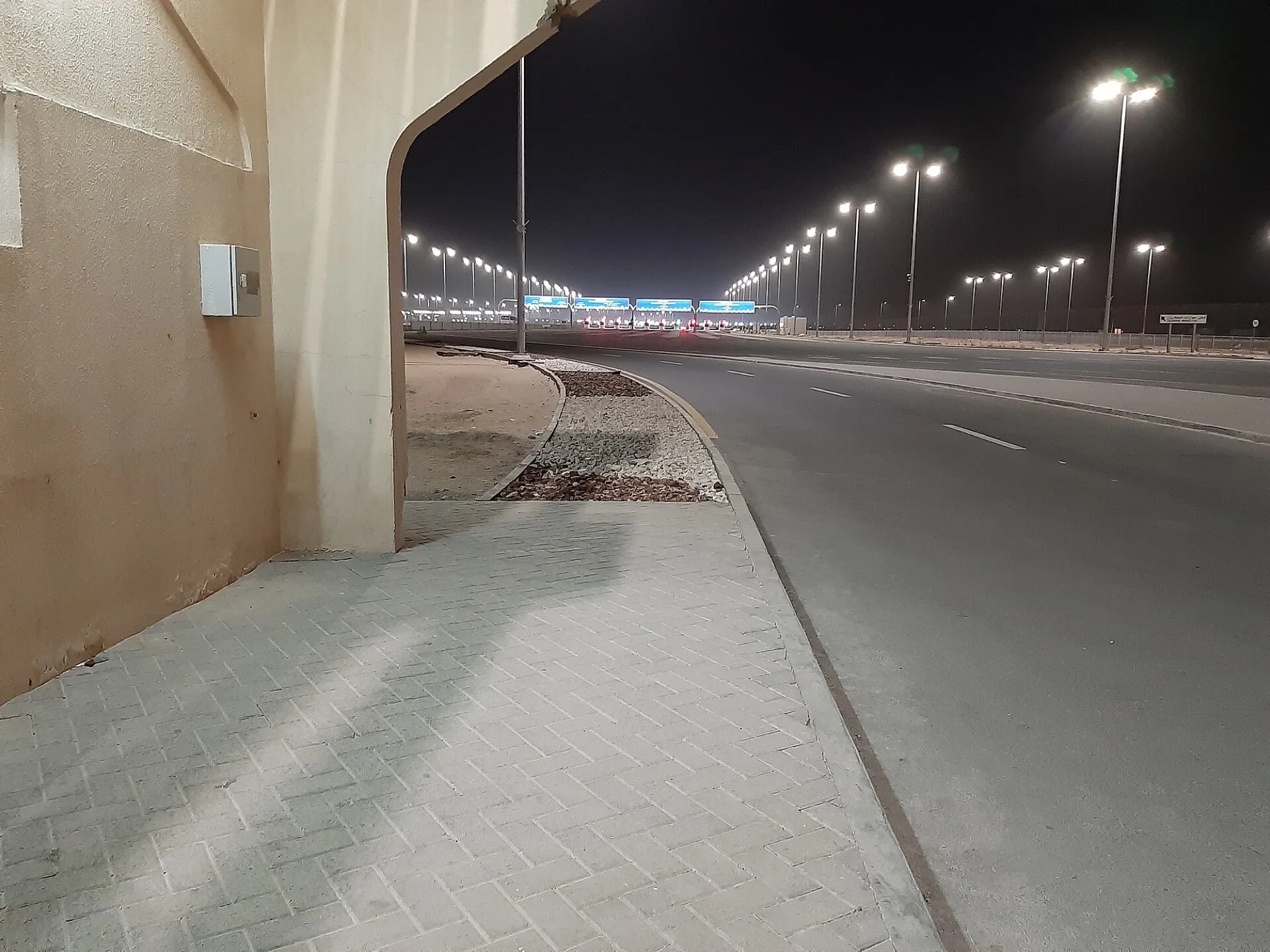 Looking down the approach road to the Al Ghuwaifat border gates at night, with a UAE border building arch on the left