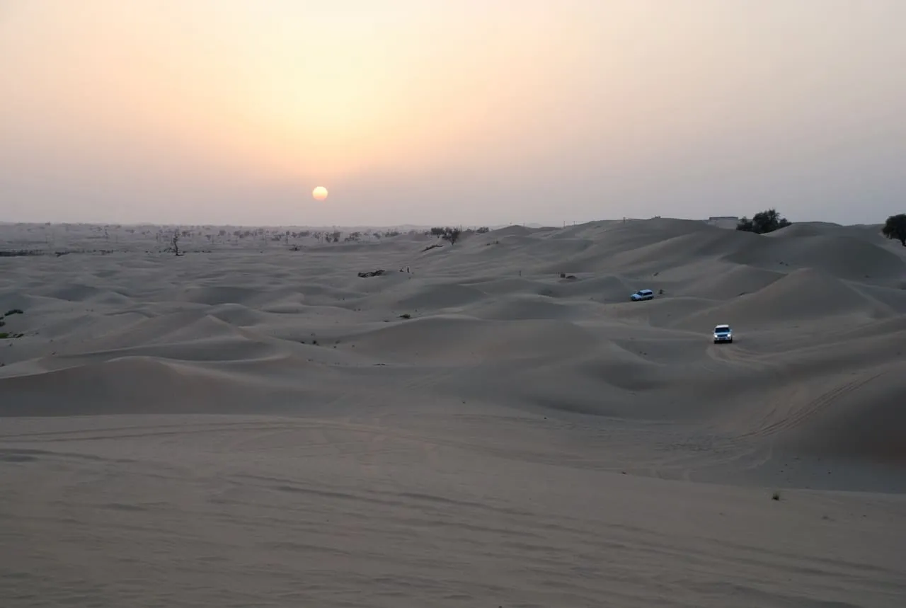 Two 4x4s crossing pale sand dunes at sunset near Sweihan, in the desert of Abu Dhabi emirate