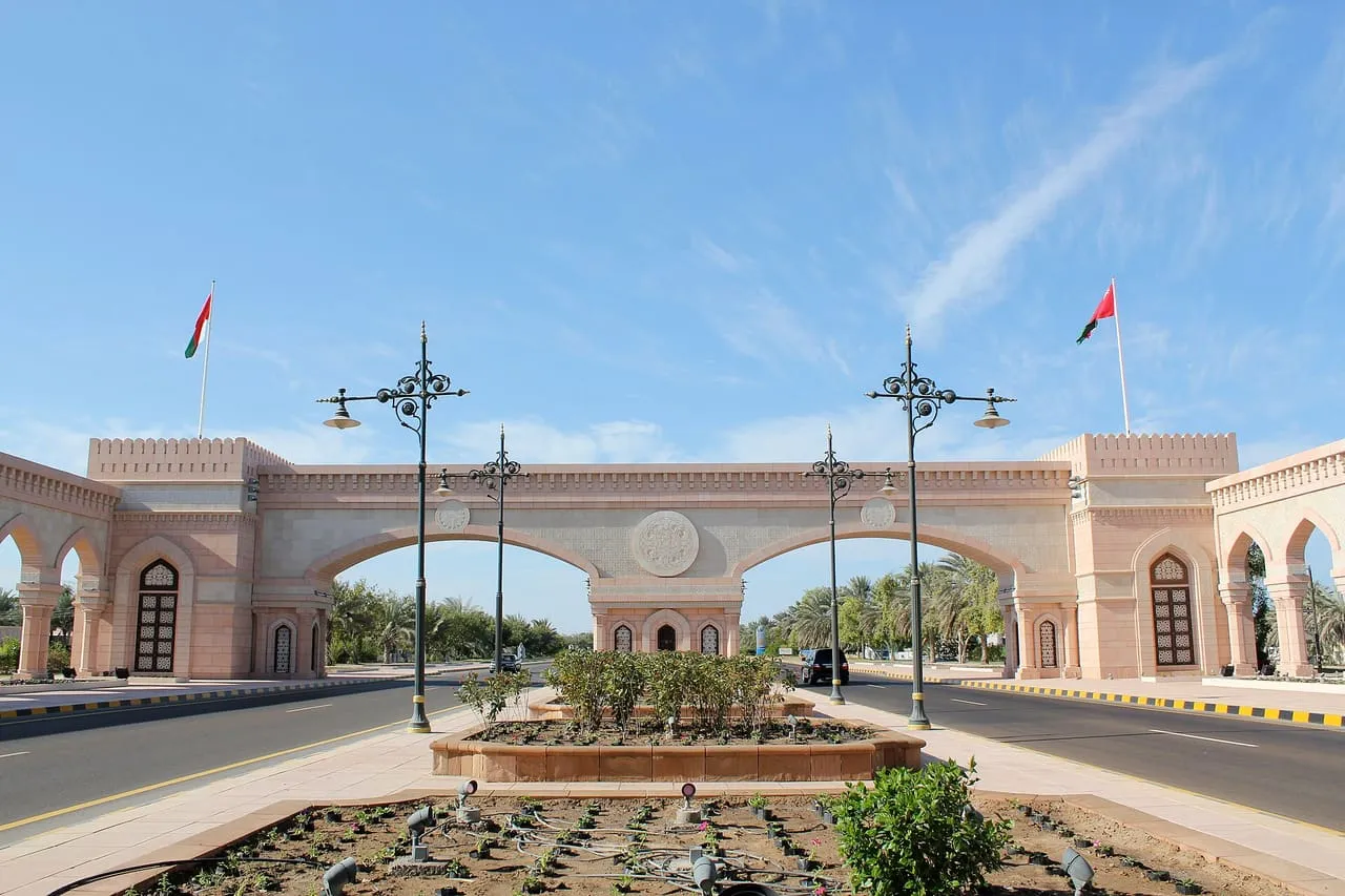 Sohar Gate, a pink stone arch with Omani flags on its towers, spanning a palm-lined road in Sohar