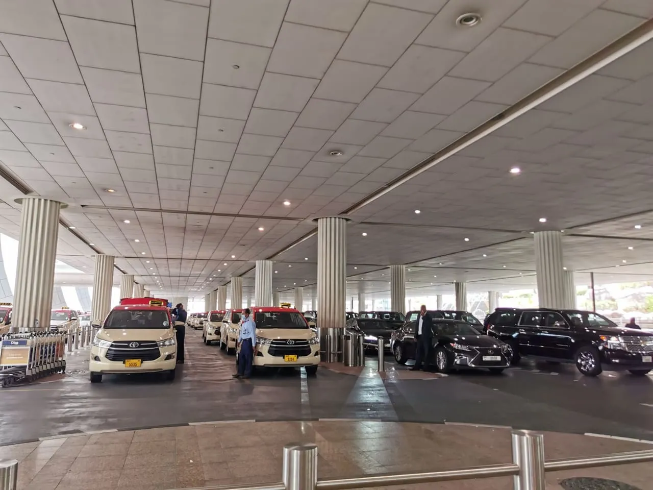 Dubai Taxi cars and black limousines waiting under the arrivals canopy at Dubai International