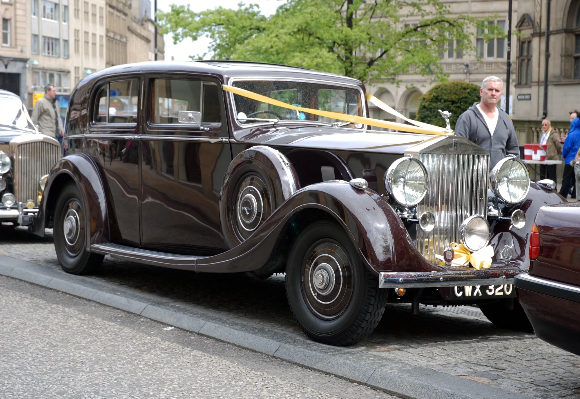 A dark maroon vintage Rolls-Royce with yellow ribbons across the bonnet, parked as a wedding car