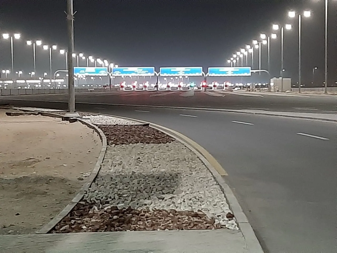Lit inspection lanes under blue gantry signs at the Al Ghuwaifat border post at night