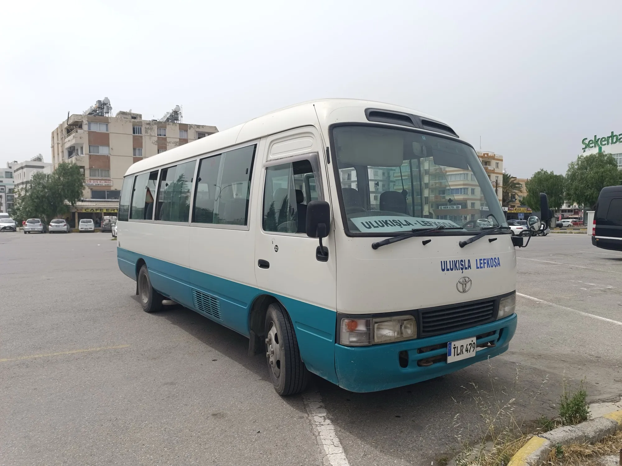 A white and teal Toyota Coaster minibus parked in a car park, the 22-seat size used for wedding hotel loops