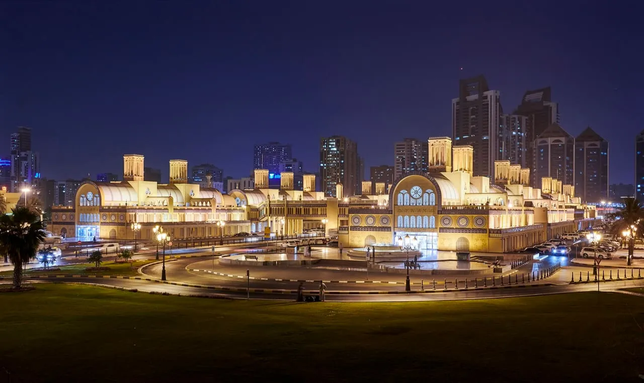 The Central Souq in Sharjah lit up at dusk, with tower blocks behind it