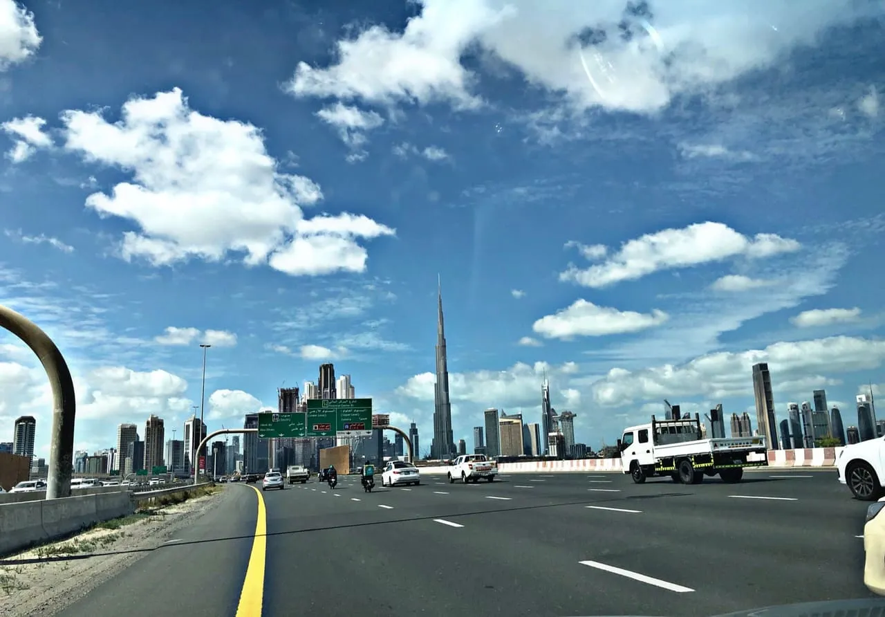 Traffic on Al Khail Road in Dubai, with direction signs for Jebel Ali and Abu Dhabi and Burj Khalifa on the skyline ahead