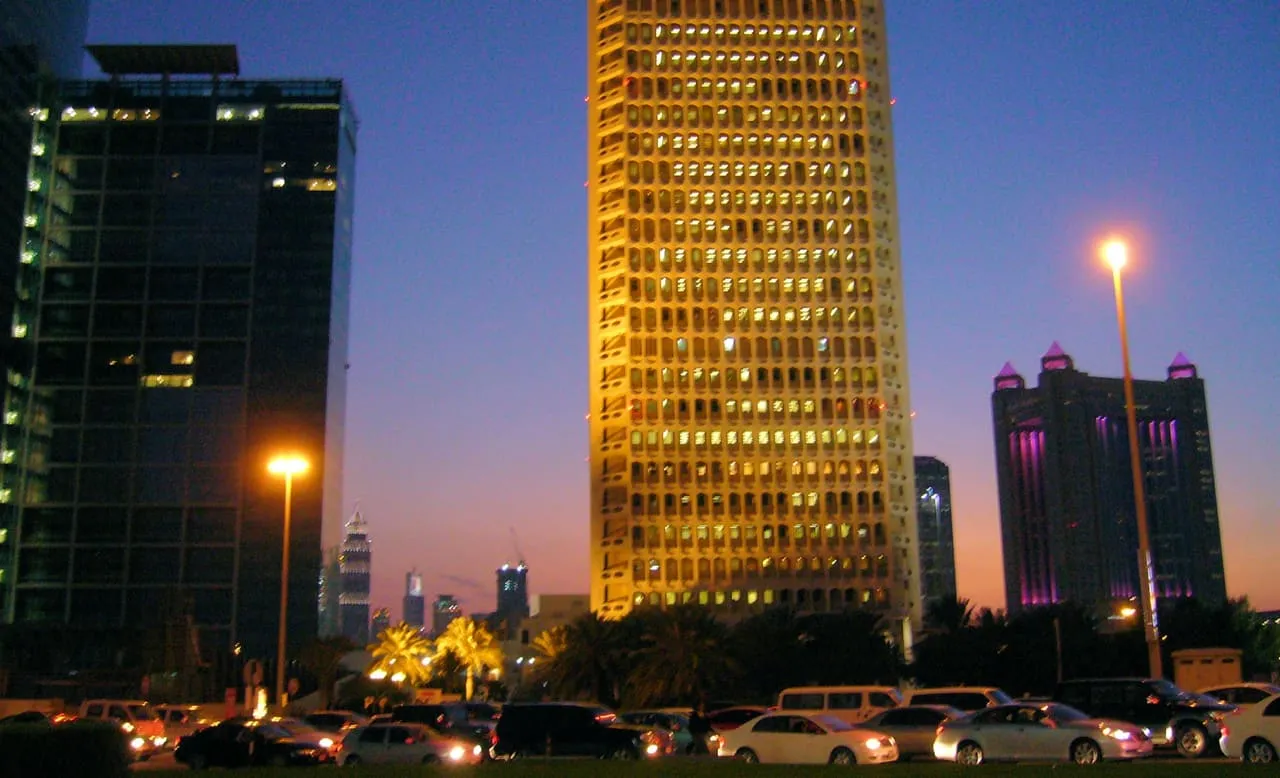The original World Trade Centre tower in Dubai lit up at dusk, with cars on the road in front