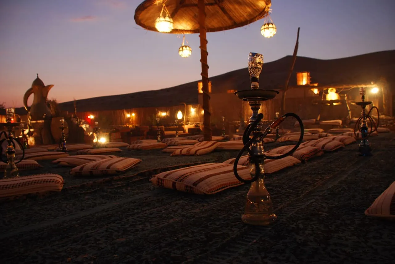 Floor cushions, lanterns and shisha pipes laid out at a desert camp outside Dubai at dusk