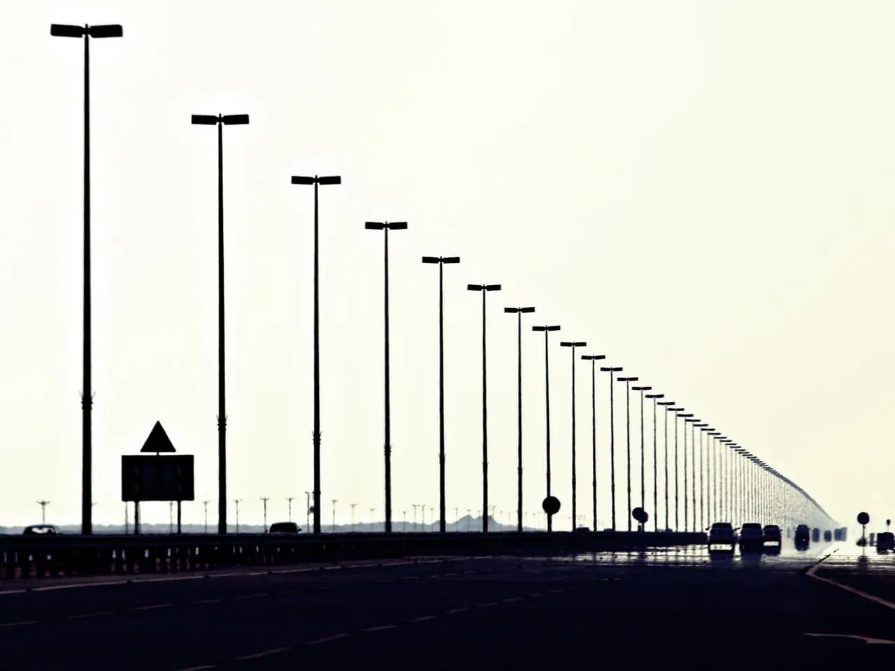 Tall lamp posts lining the Dubai to Abu Dhabi freeway, with traffic silhouetted against a pale sky