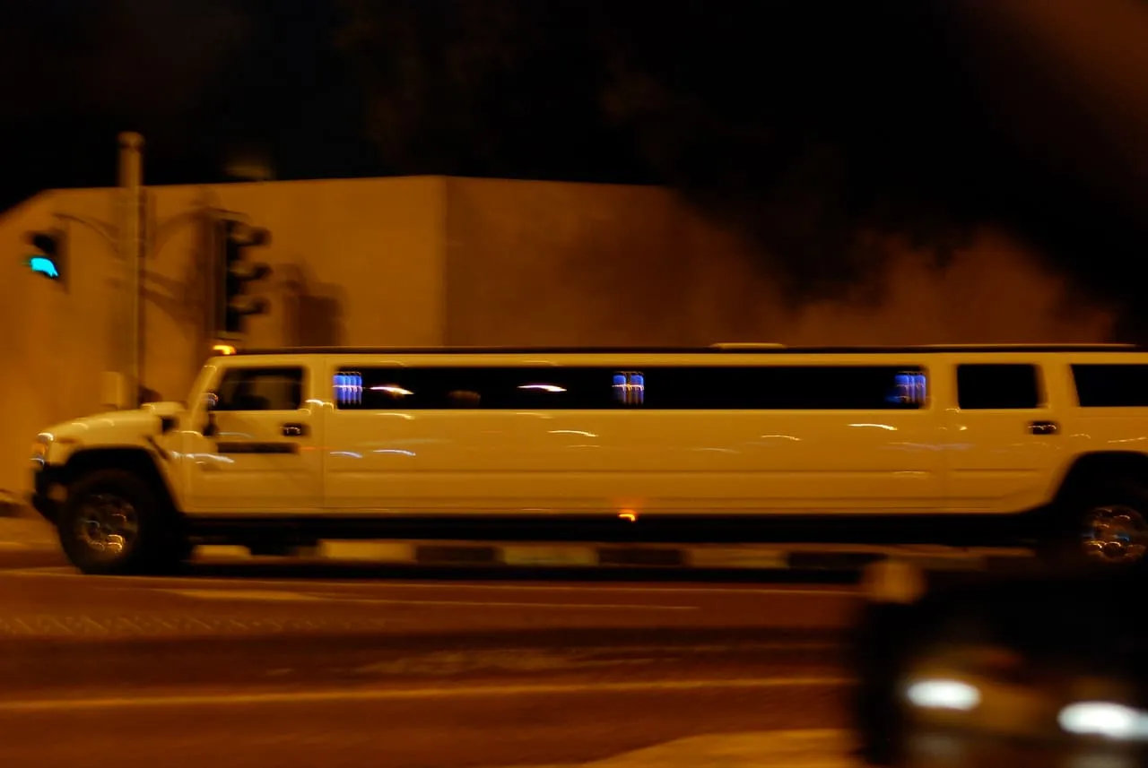 A white Hummer H2 stretch limousine driving past a traffic light on a city street at night