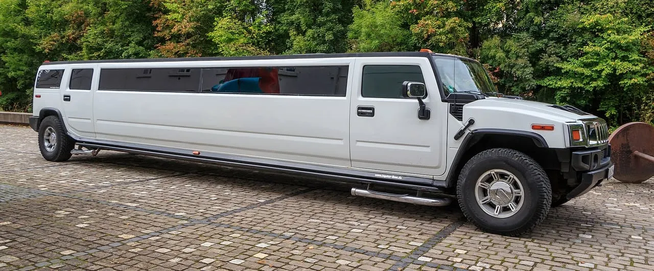 A white Hummer H2 stretch limousine with a long row of tinted side windows, parked on a cobbled square
