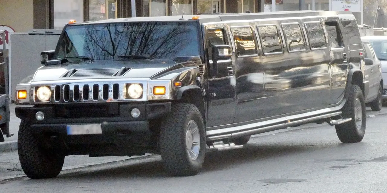 A black Hummer H2 stretch limousine parked at the kerb, with a long row of tinted side windows along the lengthened cabin