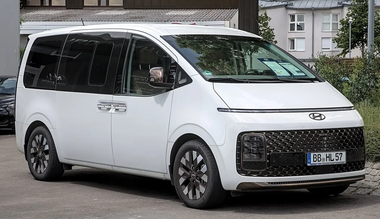 A white Hyundai Staria van with a full-width light bar across the front, seen from the front right