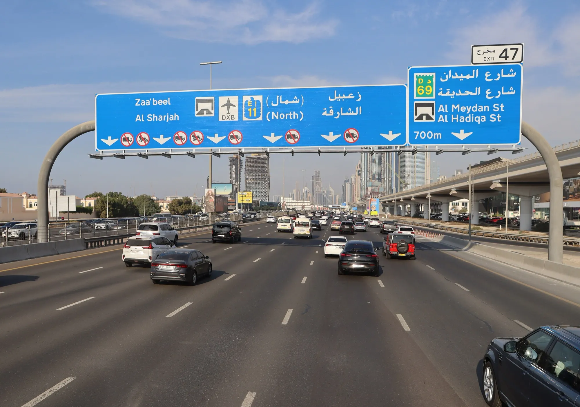 Traffic on Sheikh Zayed Road in Dubai under an overhead sign for Exit 47, Al Sharjah and Dubai International Airport