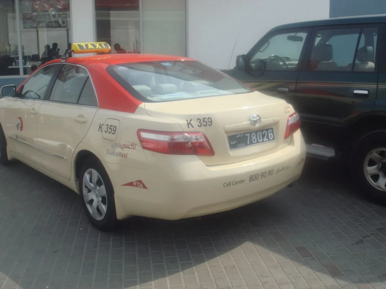 A cream Dubai Taxi Toyota Camry with a red roof and a yellow taxi sign