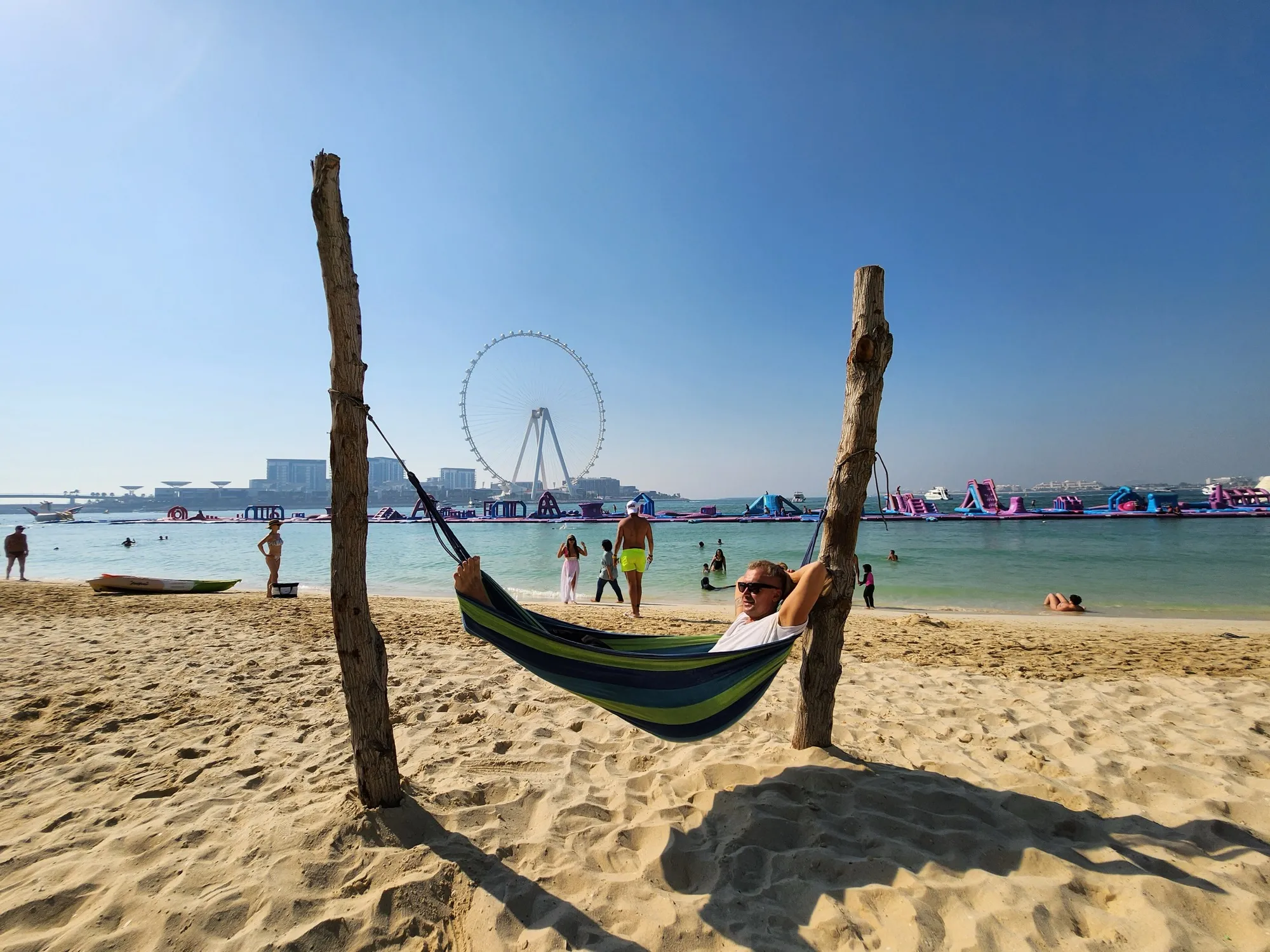 Families on the sand at JBR beach with the Ain Dubai wheel and floating water park behind