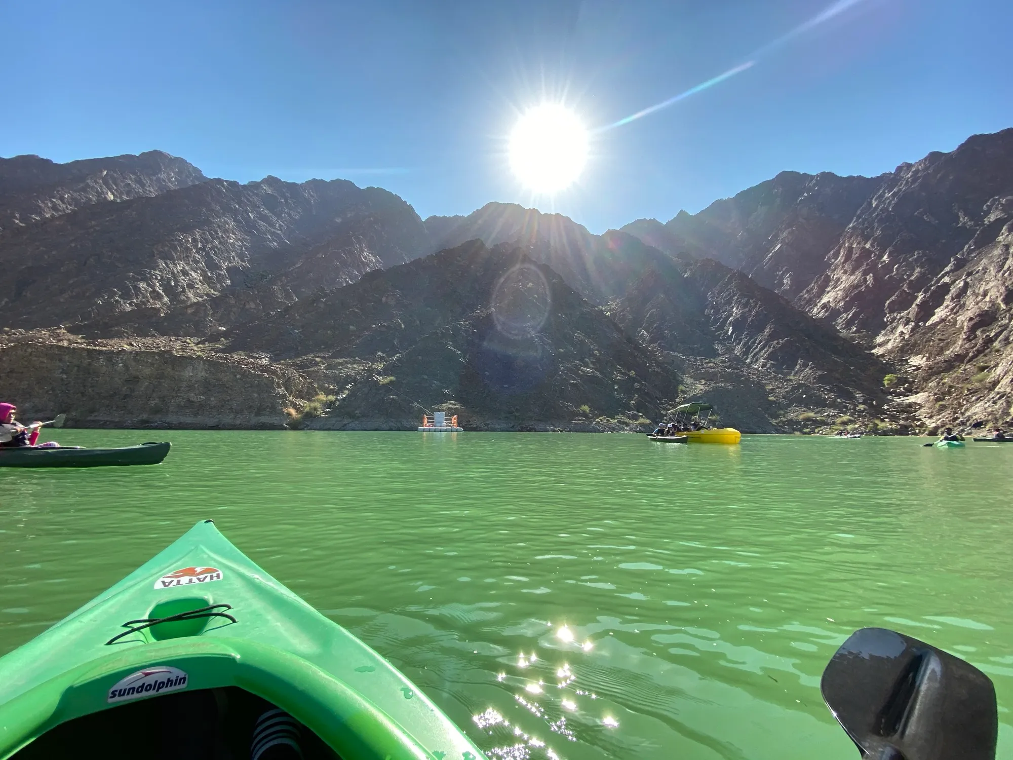A green kayak on Hatta Dam with the Hajar mountains behind