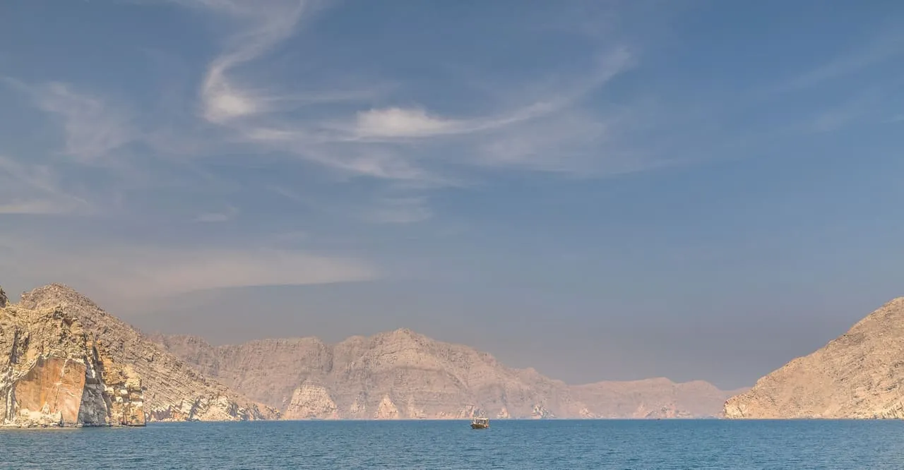 A dhow on the water in the Musandam fjords, between bare limestone mountains