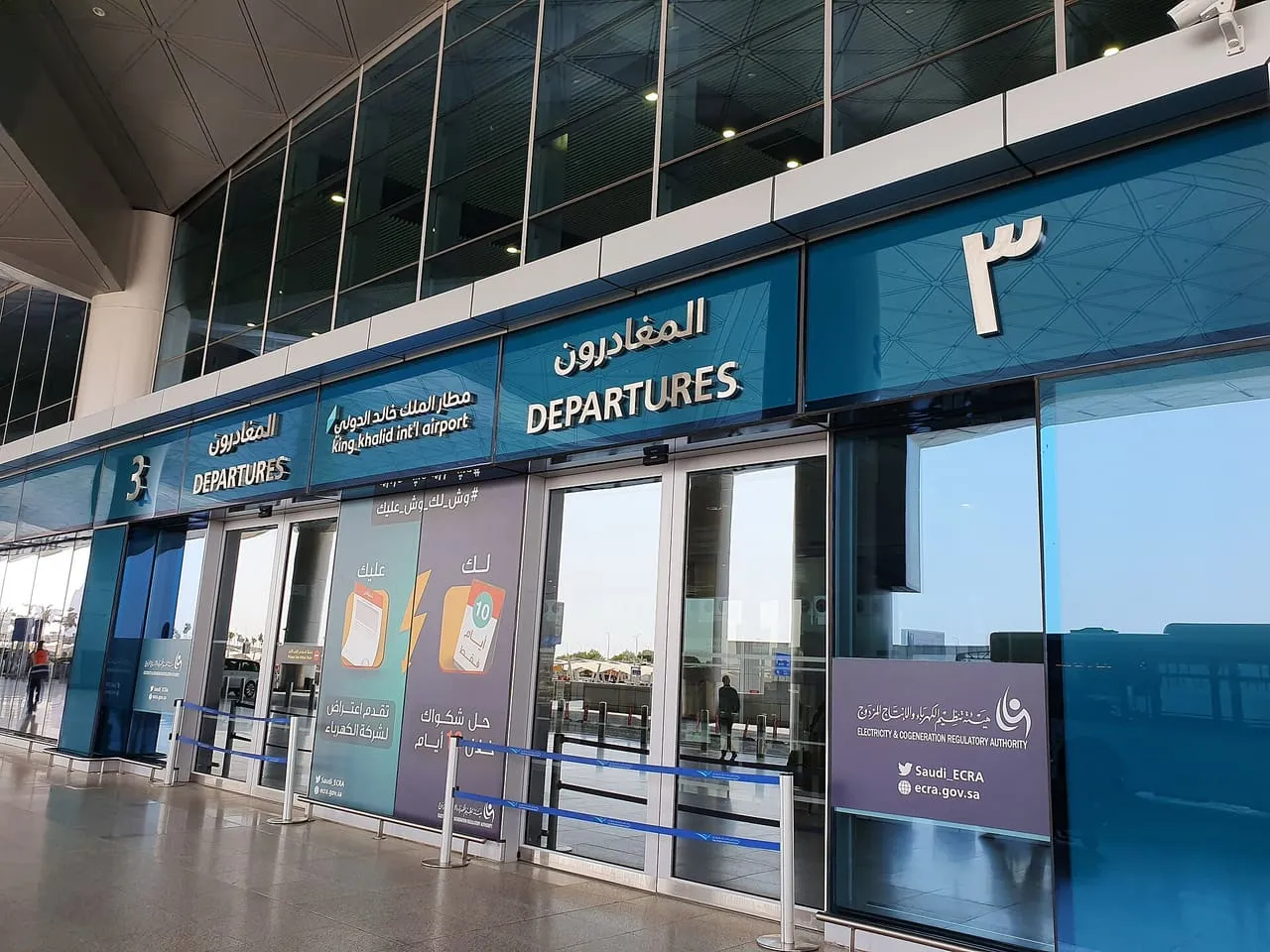 The Departures 3 entrance at King Khalid International Airport in Riyadh, with signs in Arabic and English above glass doors
