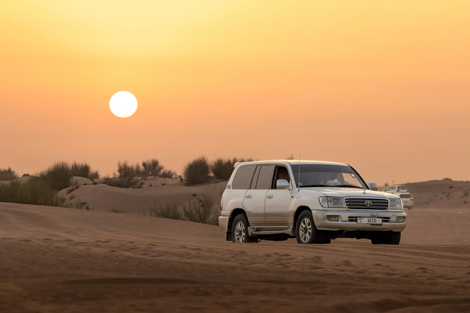 A white Toyota Land Cruiser on the dunes outside Dubai as the sun goes down