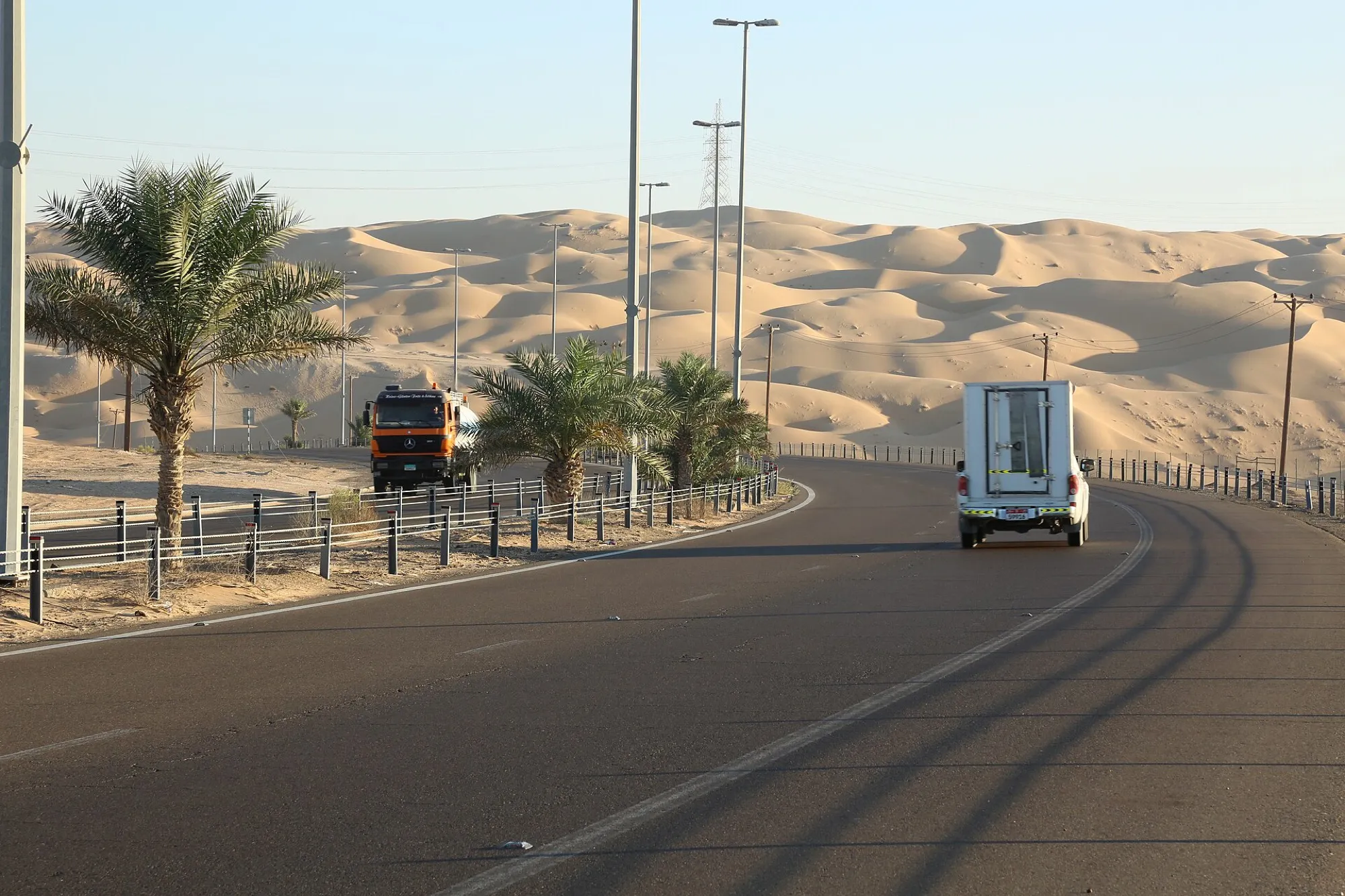 A paved desert road in the Liwa area passing date palms and tall pale sand dunes