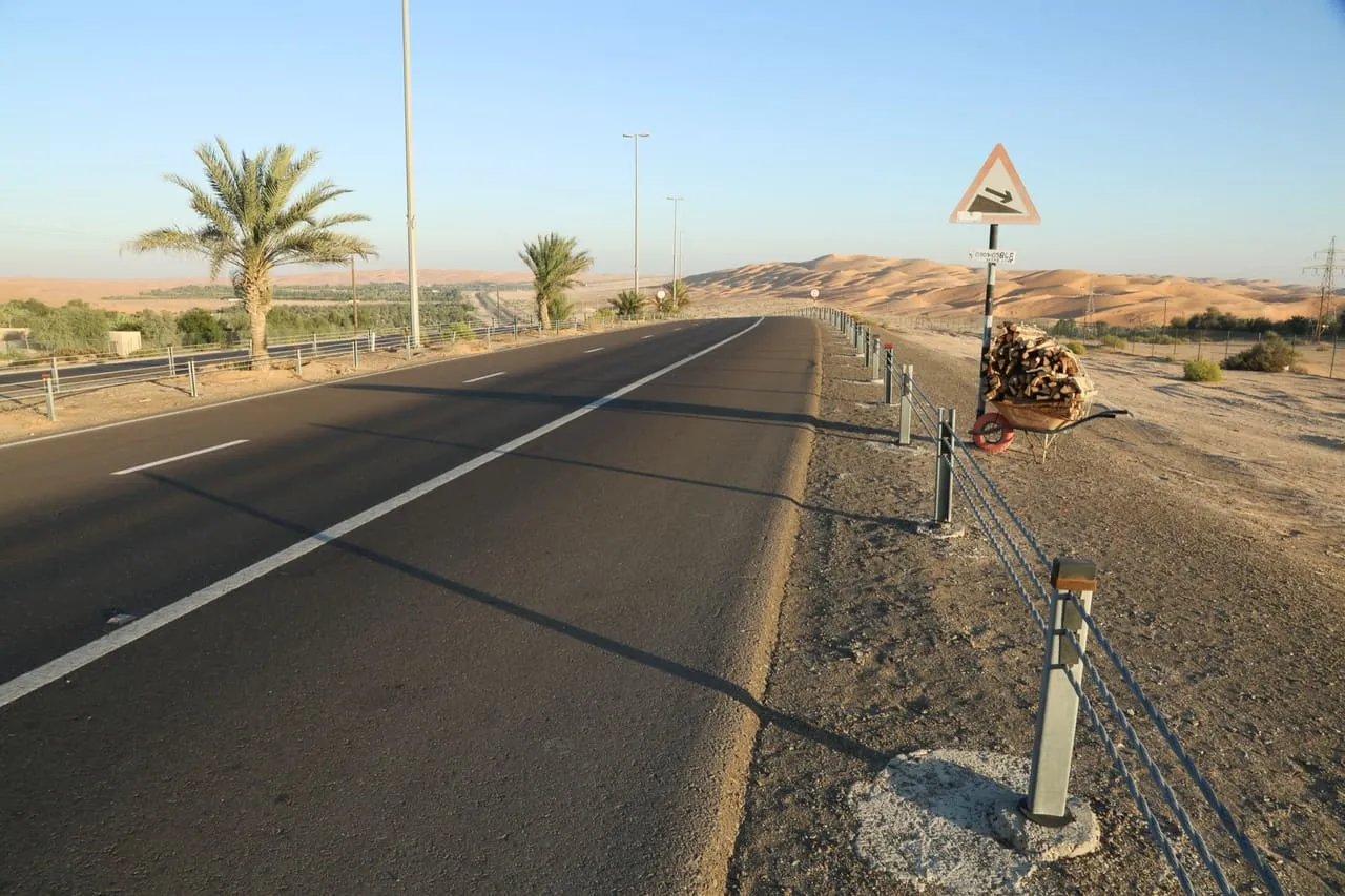 The road through Liwa, with date palms on one side and high sand dunes ahead