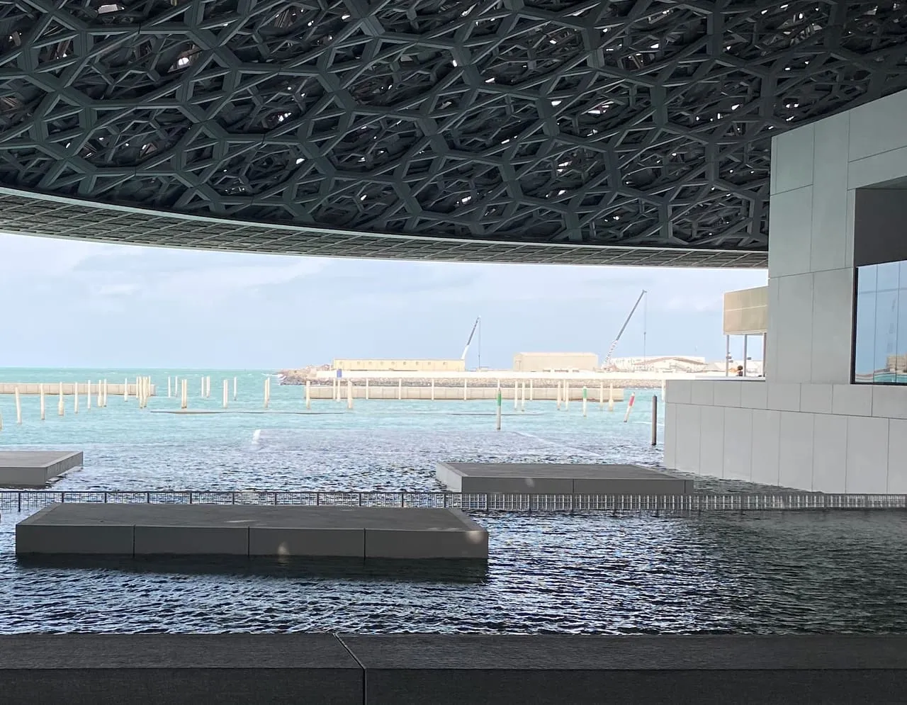 Platforms in the water under the patterned dome of Louvre Abu Dhabi, looking out to sea