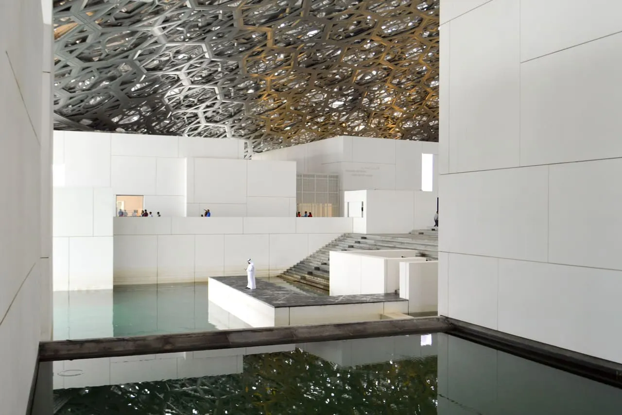 Water and white gallery buildings under the latticed dome of Louvre Abu Dhabi on Saadiyat Island