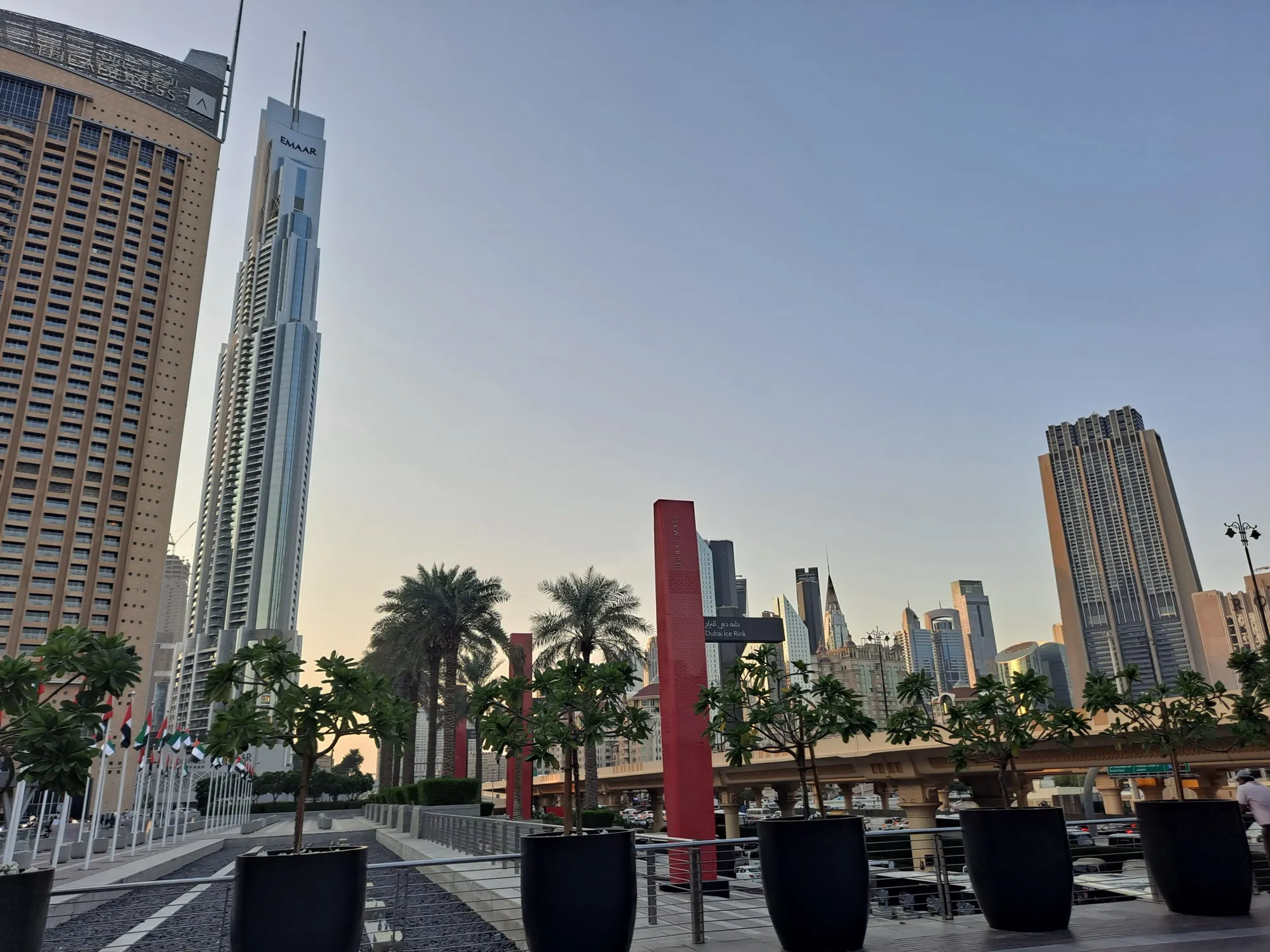 Dubai Mall’s outdoor promenade at dusk, with palms, planters and Downtown towers behind