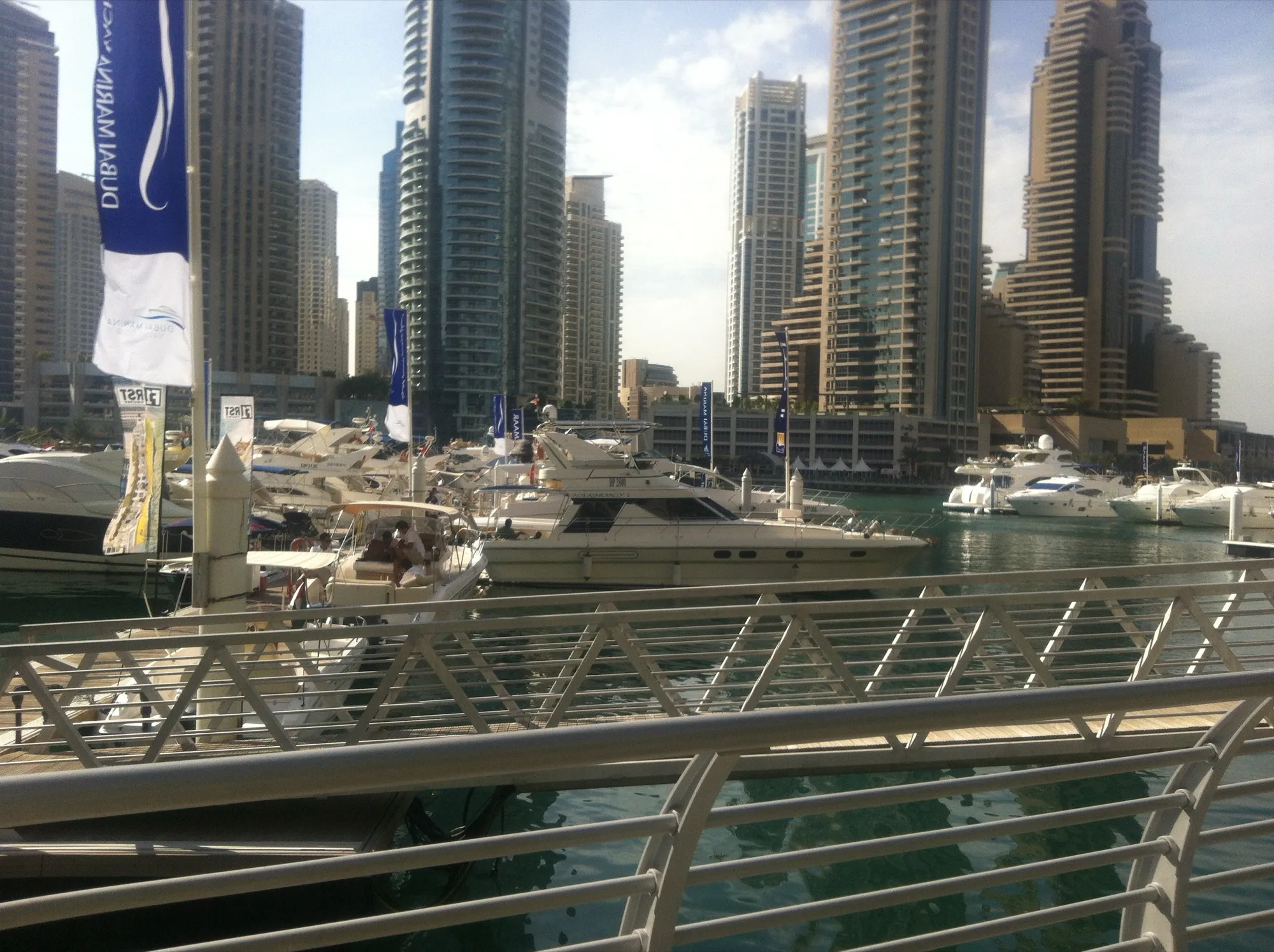 Motor yachts moored at a pontoon beside Marina Walk in Dubai Marina, with residential towers behind