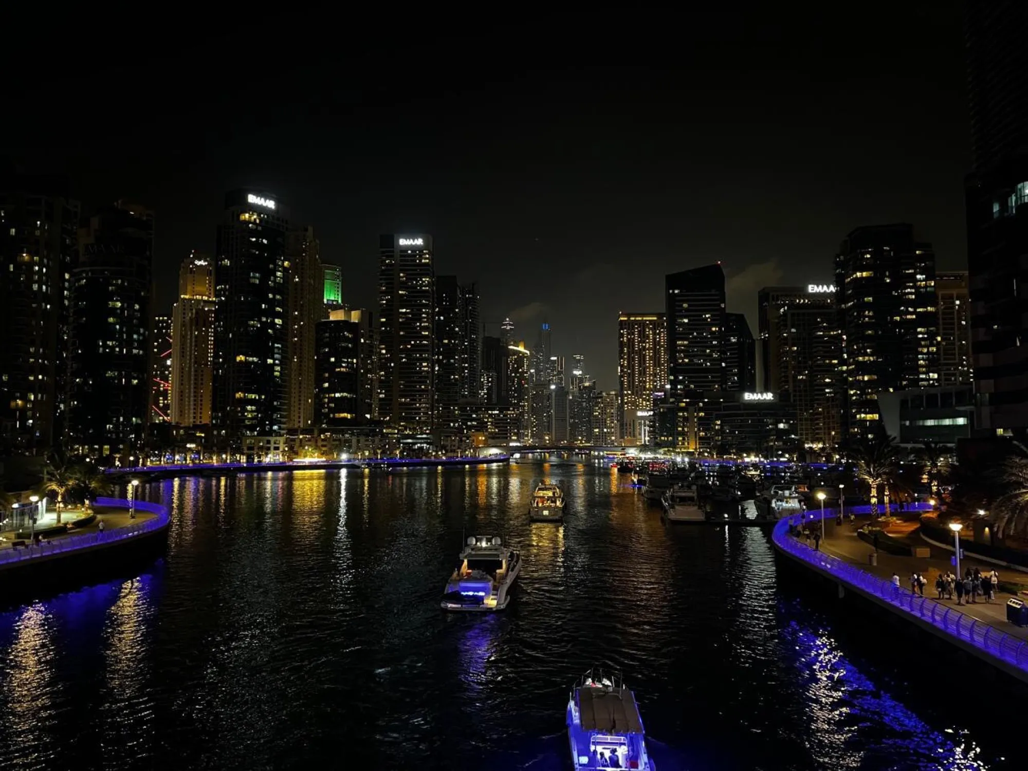 Motor yachts cruising through Dubai Marina at night between lit towers and the waterfront promenade