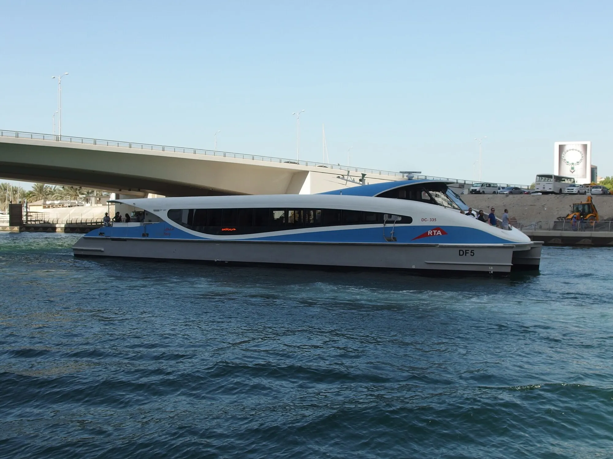 An RTA Dubai Ferry catamaran passing under a bridge