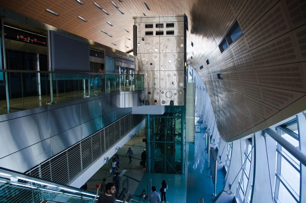 The curved interior of an above-ground Dubai Metro station, with escalators and a lift between levels