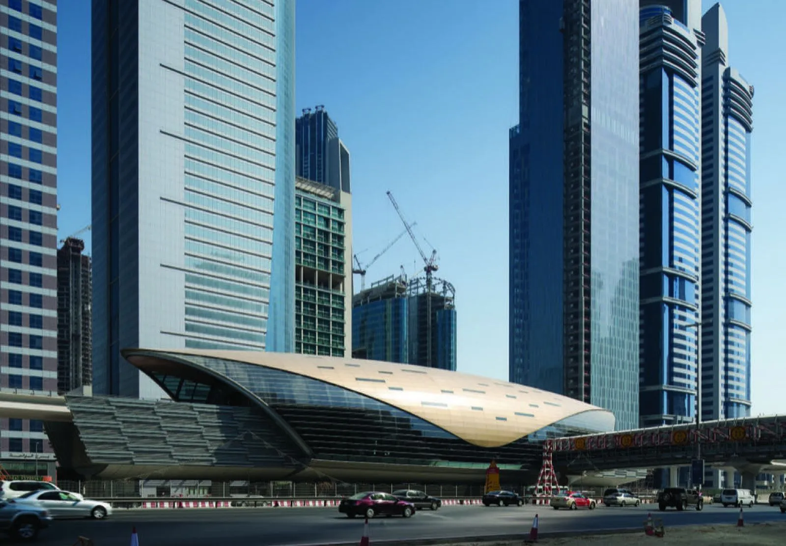 A curved Dubai Metro station building beside Sheikh Zayed Road, with office towers behind and traffic below