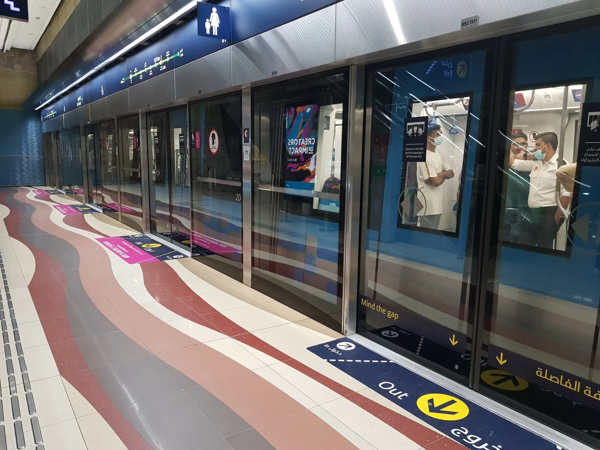 A Dubai Metro station platform with glass platform doors, floor markings and the line map above the doors