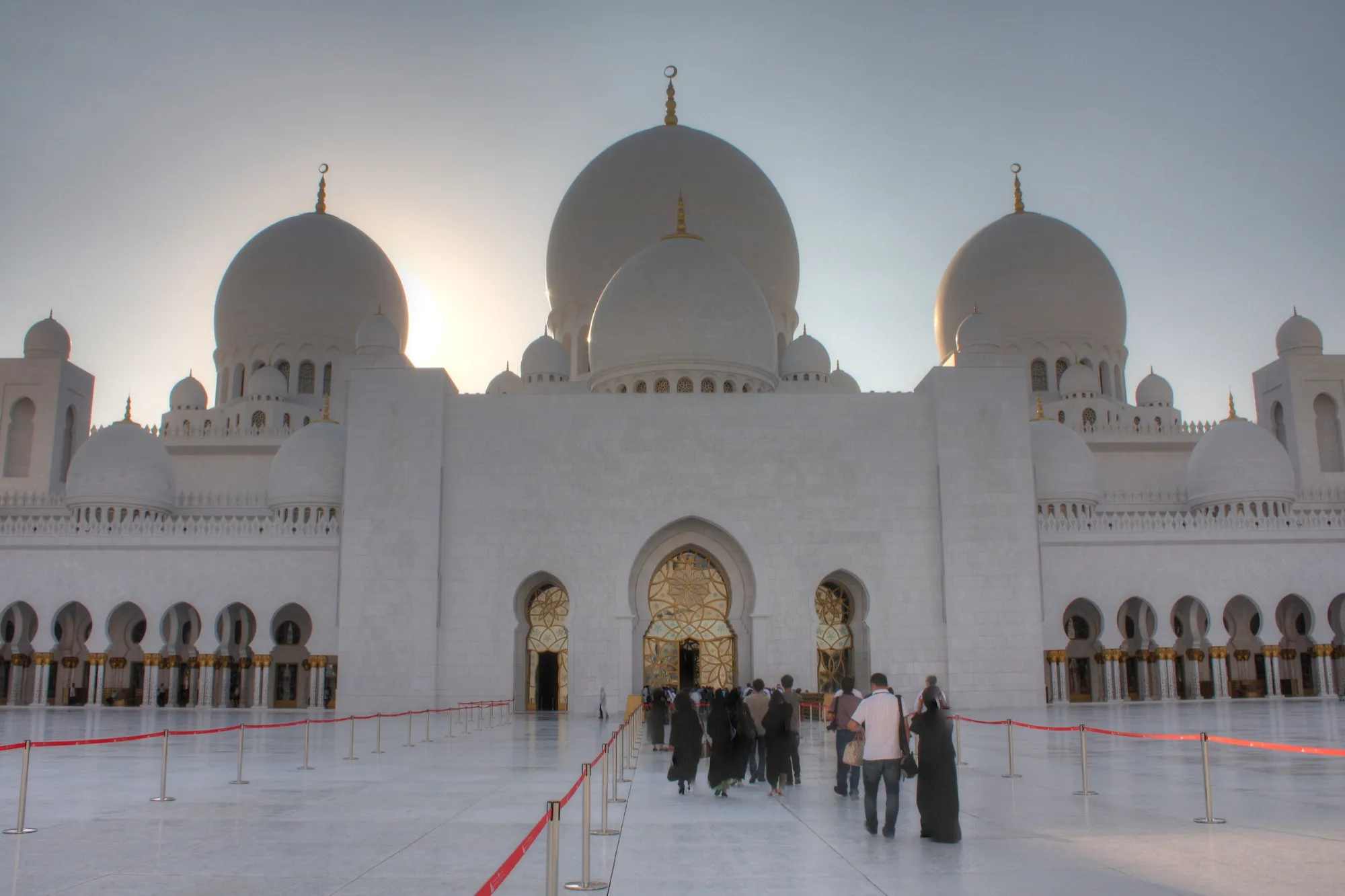 Visitors crossing the marble courtyard towards the main prayer hall entrance of the Sheikh Zayed Grand Mosque