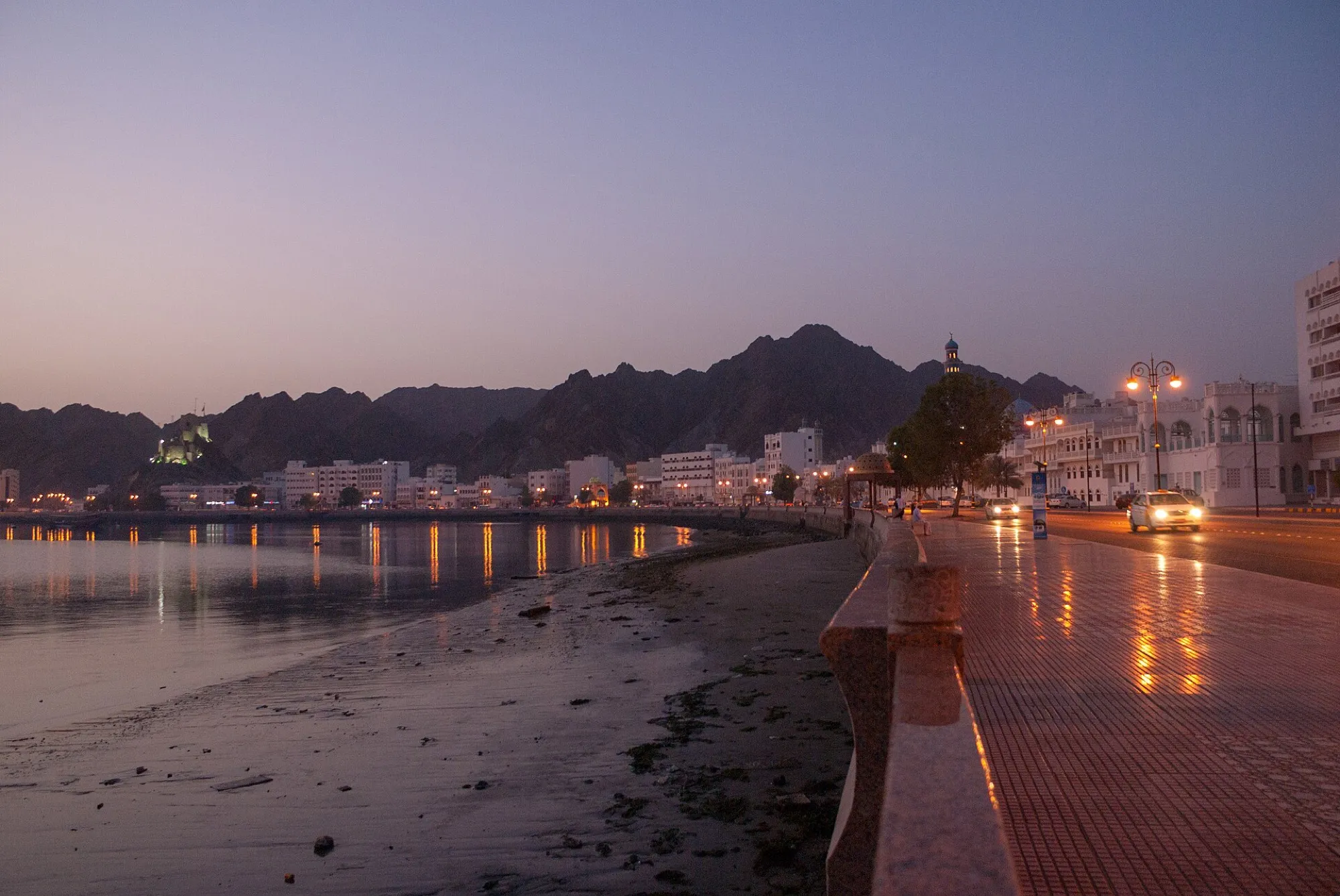 Muscat's Mutrah corniche at dusk, with the fort on the hill and the mountains behind