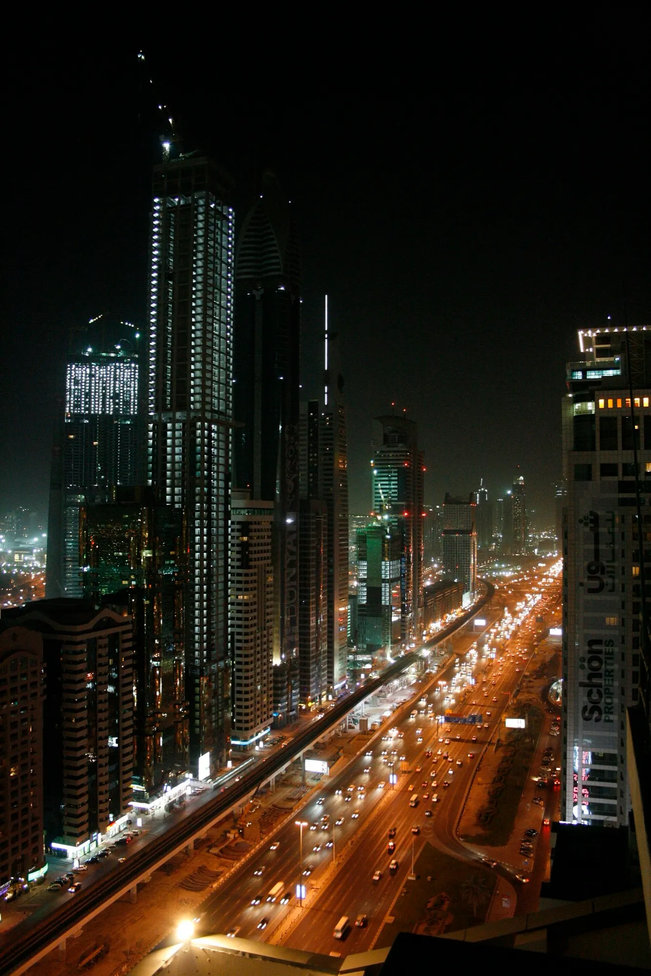 Sheikh Zayed Road in Dubai at night, with lit towers and traffic streaming along the Metro viaduct